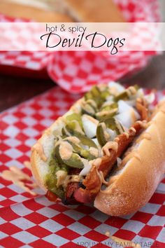 a hot dog with toppings sitting on top of a red and white checkered table cloth