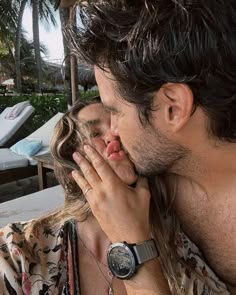 a man and woman kissing each other in front of a pool with lounge chairs behind them