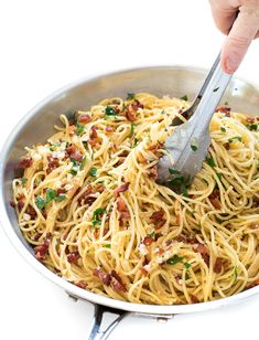 someone is using a fork to stir spaghetti in a pan with bacon and parsley