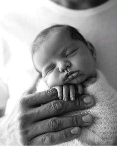 a black and white photo of a baby sleeping on its mother's lap with her hands