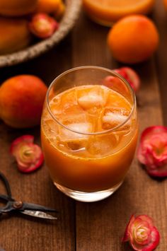 an orange drink in a glass with ice and fruit on the table next to it