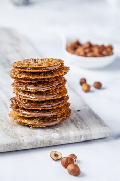 a stack of cookies sitting on top of a wooden cutting board next to some nuts