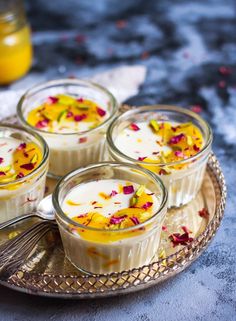 four small desserts with flowers in them sitting on a silver platter next to a jar of orange juice