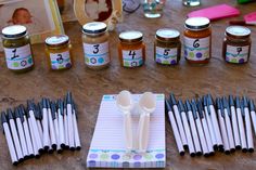 a table topped with lots of jars and spoons next to some writing utensils