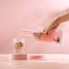 a person is pouring water into a glass with strawberries in it on a pink surface