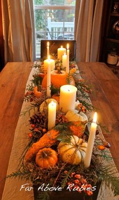 a table topped with candles and pumpkins on top of a wooden dining room table