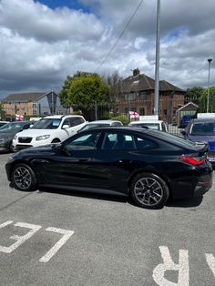 a black car parked in a parking lot next to other cars and buildings on a cloudy day