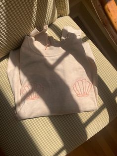 a white shirt with pink shells on it sitting on a chair