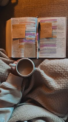 an open book on top of a bed next to a cup of coffee