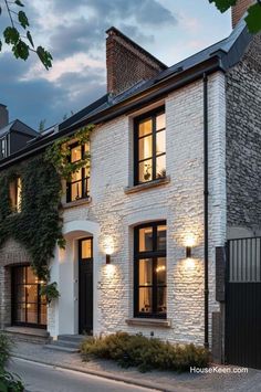 a white brick house with black shutters on the front and side windows at night