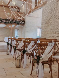 rows of wooden chairs with white sashes and flowers on them in front of a chandelier