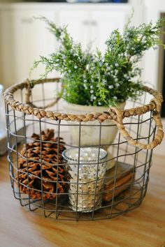 a wire basket filled with pine cones on top of a wooden table next to a potted plant