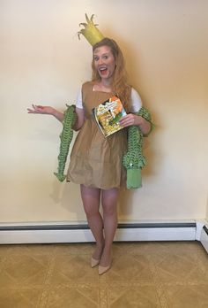 a woman wearing a costume and holding a book in one hand while standing next to a wall