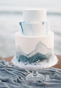 a white and blue wedding cake sitting on top of a table next to the ocean