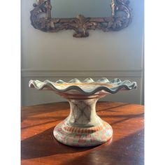 an ornate vase sitting on top of a wooden table in front of a framed mirror