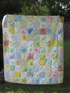 a baby quilt is hanging on a clothesline in the yard with trees and grass behind it