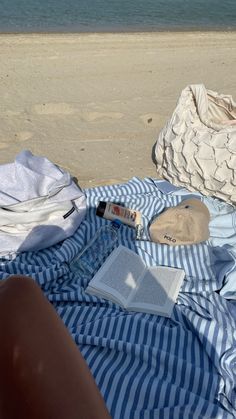 an open book on a blue and white striped blanket next to the beach with other items