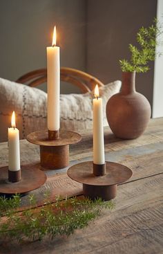 three candles sitting on top of wooden coasters in front of a vase and pillow