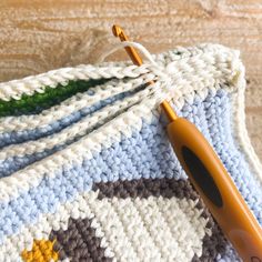 a crocheted blanket with an orange handled knitting needle resting on top of it