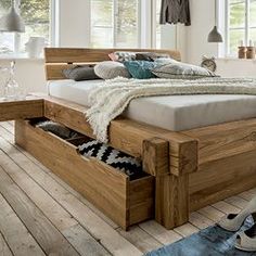 a wooden bed with drawers underneath it in a room filled with wood floors and windows