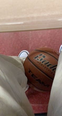 a basketball sitting on top of a red floor next to a white bag and some shoes