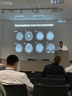 a man is giving a presentation in front of an audience with mri images on the wall