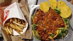 a container filled with food next to a pile of french fries and tortilla chips