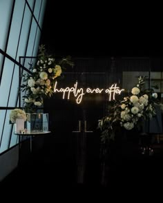 a neon sign that says happily ever after with flowers and greenery in front of it