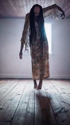 a woman with dreadlocks walking across a wooden floor in front of a window