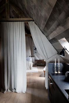 an attic bedroom with wood floors and white drapes hanging from the ceiling, next to a kitchen island