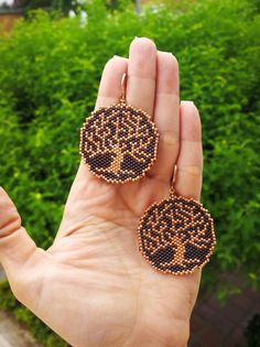 a hand is holding two beaded earrings in front of some bushes and trees on the other side