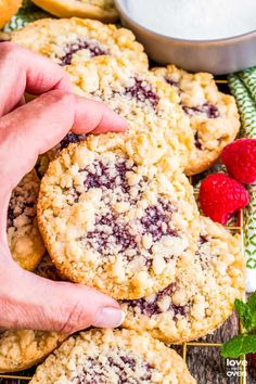 a person picking up a berry crumb cookie from a cooling rack with fresh raspberries