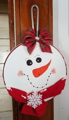 a door hanger with a snowman face painted on it and a red bow