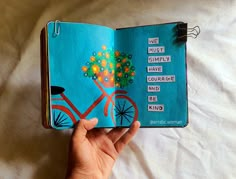 a hand holding an open book with words on the pages and a bicycle painted on it