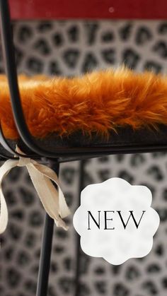 Image of a black metal kitchen bar stool with a mustard yellow sheepskin seat pad / seat cushion on, with black and white animal print in the background and the word new. Baa Stool.