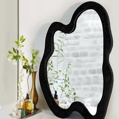 a mirror sitting on top of a counter next to a vase and potted plant