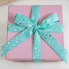 a pink gift box with blue and silver stars on it, tied with a green ribbon