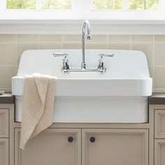 a white kitchen sink sitting under a window next to cupboards and towels on the counter