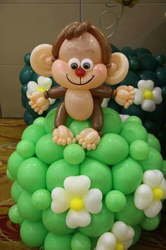 a balloon monkey sitting on top of a bunch of green and white balloons in the shape of flowers