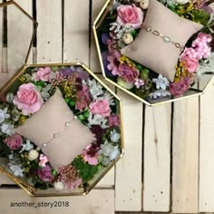 two gold trays filled with pink and white flowers sitting on top of a wooden table