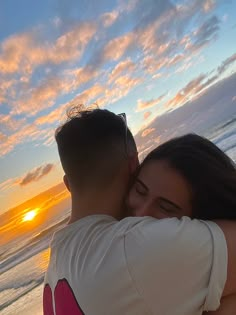 a man and woman hugging on the beach at sunset