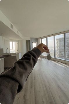 a person holding a key in an empty room with large windows and wood flooring