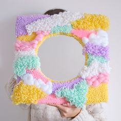 a woman holding up a colorful knitted wreath