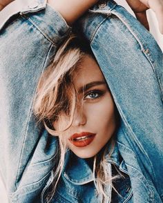 a woman with blue eyes and red lipstick is hiding her head behind a jean jacket