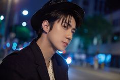 a young man in a black suit and hat standing on the side of a street at night