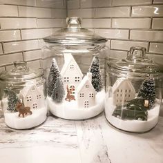 three glass jars with houses, trees and animals in them on a marble countertop