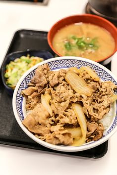 a bowl of food with meat and vegetables in it on a tray next to a bowl of soup