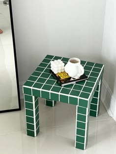 a green table with a white coffee cup on it next to a mirror and vase