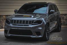 the front end of a gray jeep parked in front of a garage with stone walls