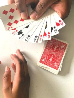 two hands holding playing cards on top of a table